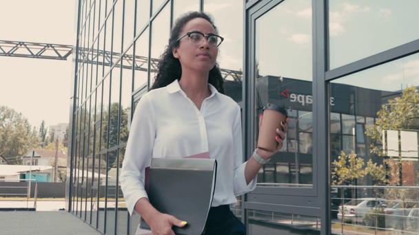 Donna d'affari afroamericana con documenti e bicchieri di carta sulla strada urbana - Filmati, video