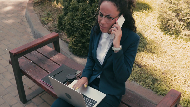 Afrikanisch-amerikanische Geschäftsfrau spricht auf Smartphone auf Bank in der Stadtstraße - Filmmaterial, Video