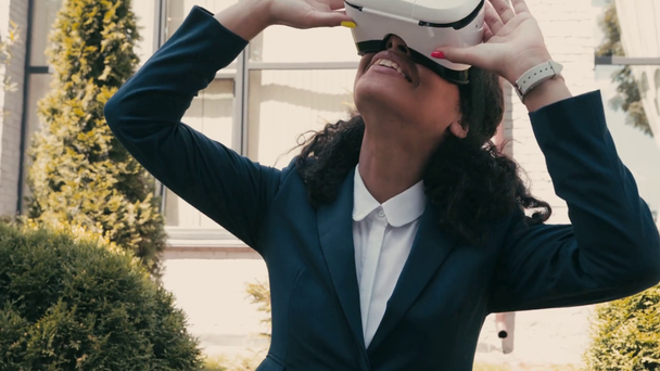 Happy african american businesswoman using vr headset on urban street  - Materiał filmowy, wideo