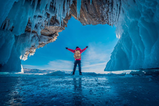 Мандрівник одягає червоний одяг і піднімає руку на замороженій воді в крижаній печері на озері Байкал (Сибір, Росія).. - Фото, зображення