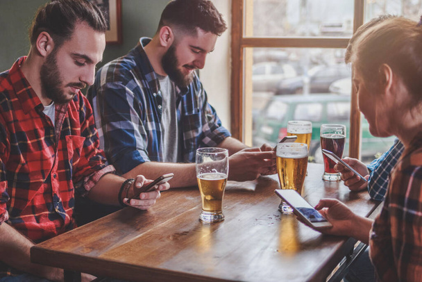 Amigos bebiendo cerveza, surfeando en smartphones y riéndose en el bar - Foto, imagen