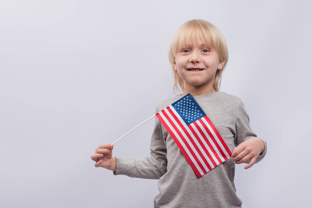 Молодий хлопчик тримає американський прапор на білому тлі. Вивчення американської англійської. - Фото, зображення