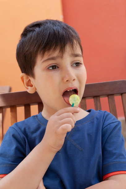 幸せな子供時代のコンセプト。かわいい男の子食べるロリポップキャンディーと楽しい屋外を持っている - 写真・画像
