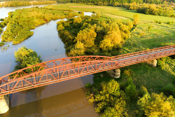 緑豊かな農村部の泥だらけの広い川にまたがる細い道路橋の空中写真. - 写真・画像