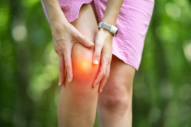 Женщина держит колено руками, испытывая сильную боль.. - Фото, изображение