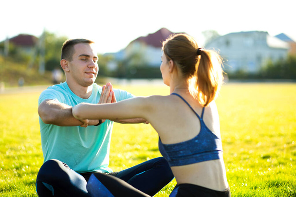 Young sportive couple doing yoga fitness exercises on warm summer day outdoors. - Foto, afbeelding