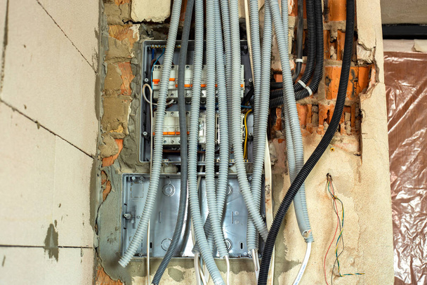 Kable elektryczne umieszczone w ochronnej fali montowane na suficie i ścianie w pomieszczeniu w trakcie prac budowlanych. - Zdjęcie, obraz