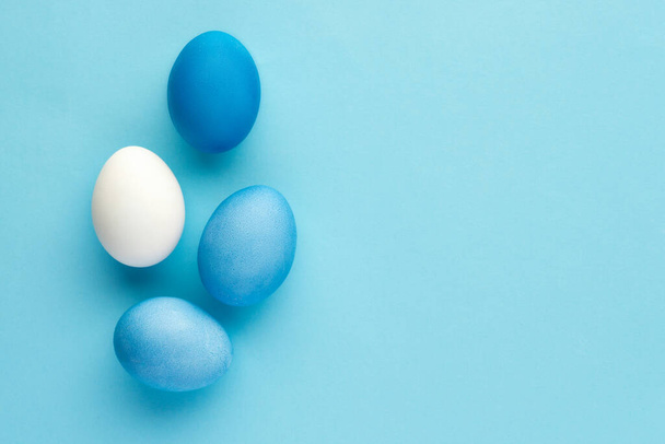 Blue painted eggs with white natural egg on blue background, monochrome top-view  - Foto, Bild