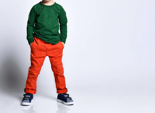 Cropped photo of a boy in a green jumper, orange pants, blue sneakers. He put his hands in his pockets, posing isolated on a white background. Childhood, fashion, advertising. - Fotoğraf, Görsel