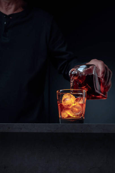 A csapos whiskyt öntött az üvegbe a pultnál. Alkoholos ital, ami egy üvegből egy jéggel teli, cukormázas pohárba folyik. Szelektív fókusz, másolás. - Fotó, kép