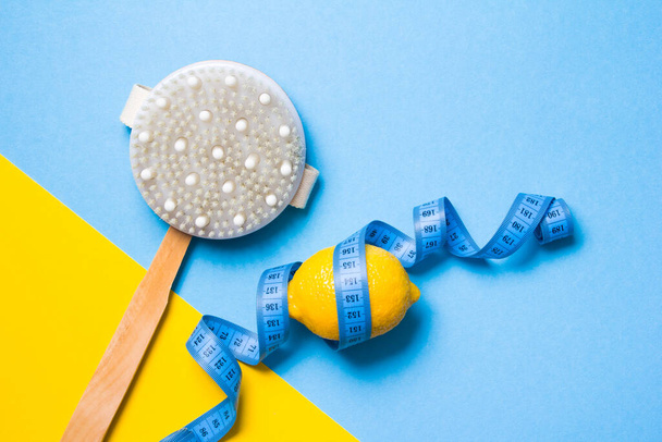 blue measuring tape, wooden brush with natural pile of cactus and lemon on a yellow and light blue background copy space top view, anti-cellulite massage concept - 写真・画像