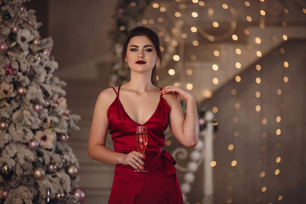 Fashionable young woman wearing luxurious evening dress and with beautiful evening makeup and hairstyle in the fairy beautiful Christmas interior. - Photo, Image