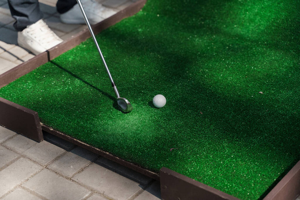 Minigolfozni a zöld füvön niblick-kel. A játékos eltalálja a fehér labdát. Golf sport játék. Golfütő hirdetés - Fotó, kép