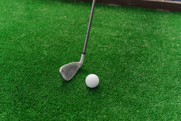 Hraní minigolf na zelené trávě pomocí niblick. Hráč odpaluje bílý míč. Golfový sport. Reklama na golfovou hůl - Fotografie, Obrázek
