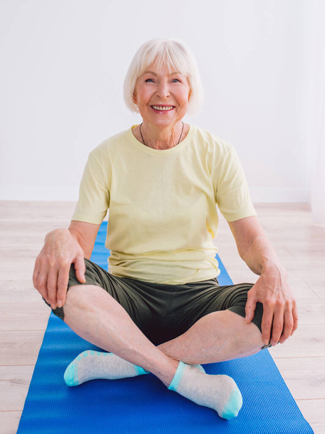 Oudere vrouw doet yoga binnen. Anti-leeftijd, sport, yoga concept - Foto, afbeelding
