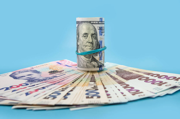 Він зібрав 100 доларів і українську гривні на синьому фоні. Фінансова концепція. - Фото, зображення