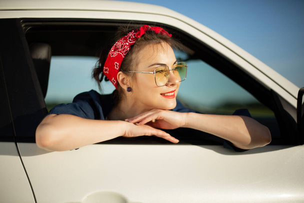 Young pretty woman leaning out of car in a summer trip. - Photo, Image