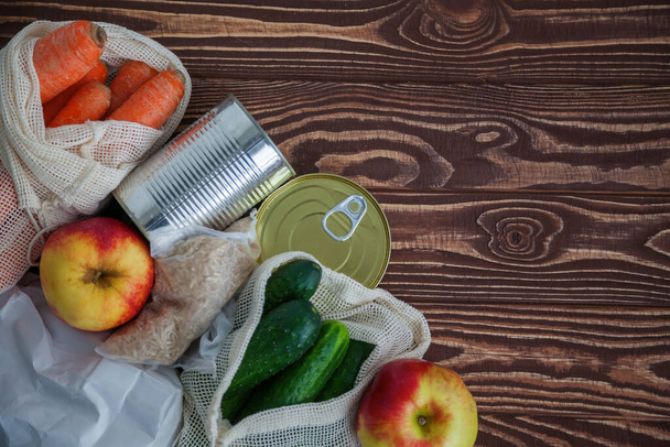 A set of different food products for home purveyance. Some of them are in reusable bags. Canned food, rice, fruits and vegetables on a wooden background. Copy-space, top view - Valokuva, kuva