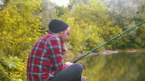 Młody człowiek siedzi na rybach - pociągając za wędkę i kręcąc ruletką - Materiał filmowy, wideo