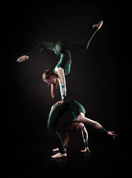 Two young female equilibrists perform acrobatic elements on a dark background in contoured lighting. - Fotografie, Obrázek
