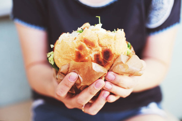 The girl is holding a big hamburger. Soft blurry background. life style - Фото, изображение