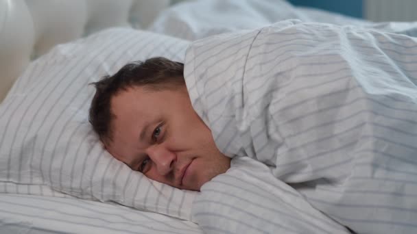 Jongeman ligt op het bed bedekt met een deken, kan niet slapen - Video