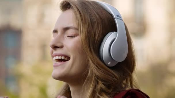 Cheerful woman relaxing in headphones outdoors. Pretty girl face listening music - Materiał filmowy, wideo
