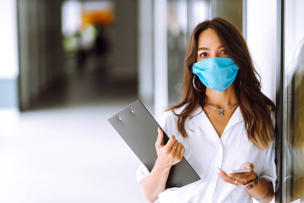 Portrait of young business woman in protective face mask at office. COVID - 19 virus protection. - 写真・画像