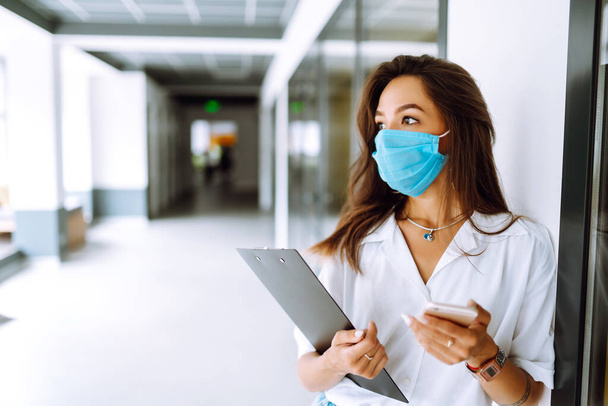 Portrait of young business woman in protective face mask at office. COVID - 19 virus protection. - Foto, afbeelding