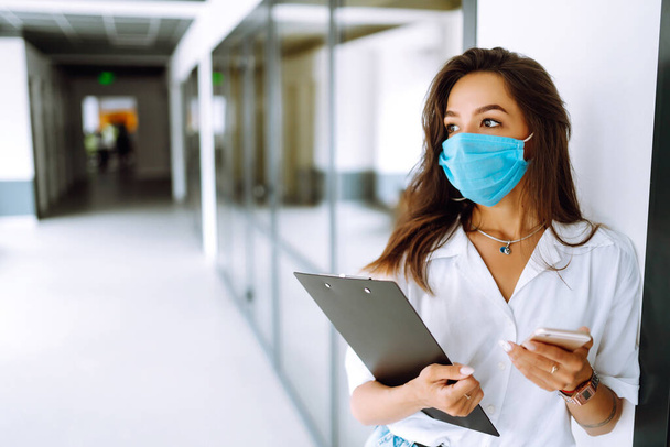 Portrait of young business woman in protective face mask at office. COVID - 19 virus protection. - 写真・画像