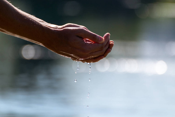 Gros plan des mains coupant l'eau de la rivière de mer avec un fond de bokeh flou. Attraper de l'eau pure dans les mains gouttes tombant dans la surface de l'eau - Photo, image