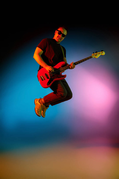 Young caucasian musician playing on gradient background in neon light. Concept of music, hobby, festival - Photo, image
