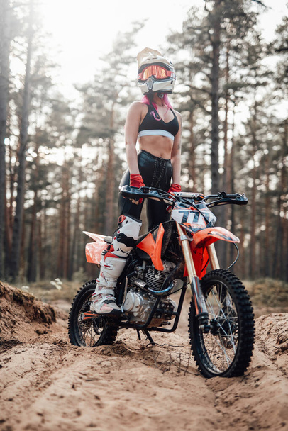 Young female motocross racer in safety helmet riding on her motorcycle in off road adventure - Photo, image