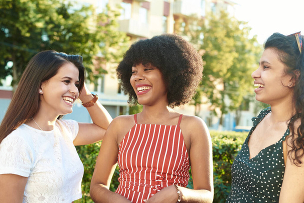 İletişim ve arkadaşlık kavramı. Farklı ırktan genç kızlar şehrin arka planında iletişim kuruyor.. - Fotoğraf, Görsel