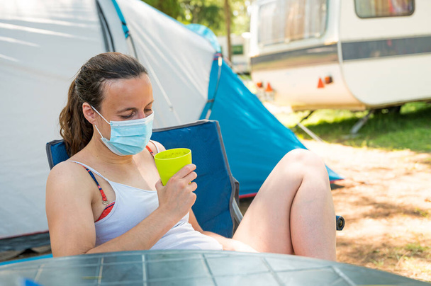 Frau mit medizinischer Maske trinkt Erfrischung im Zeltlager. - Foto, Bild