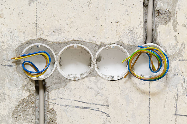 Holes in a concrete wall for installing plastic boxes under sockets. installation of sockets in a concrete wall and wiring. - Photo, Image