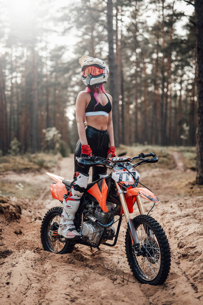 Young female motocross racer in safety helmet riding on her motorcycle in off road adventure - Photo, Image
