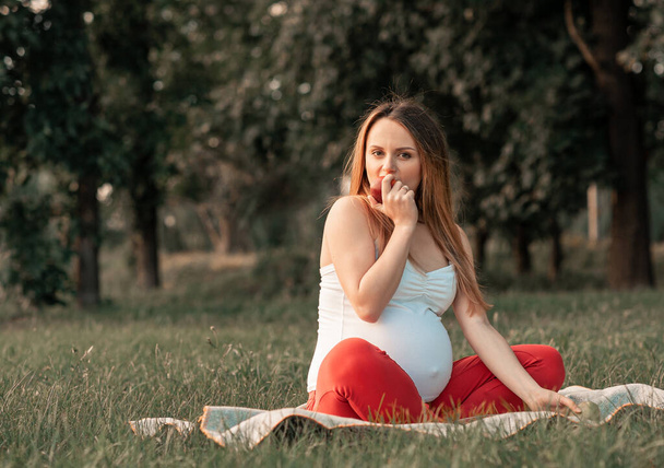 Cute pregnant woman eat apples on picnik. healthy pregnancy, pregnant young female in park summer - 写真・画像