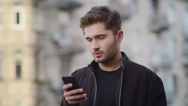 Upset man using phone outside. Annoyed guy looking screen on street. - Πλάνα, βίντεο