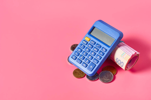 Ukrainian banknotes and metal coins near calculator on pink background - Foto, afbeelding