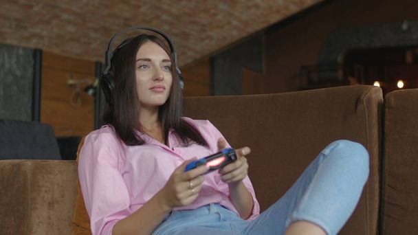 Frau mit Kopfhörer sitzt auf Sofa und spielt Videospiel - Foto, Bild