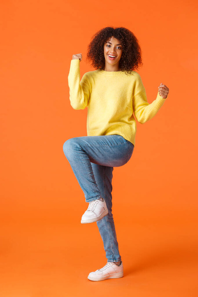 Full-length vertical shot happy lucky african-american female student with afro haircut, got sholarship feeling like champion, fist pump and lift leg in celebration, do triumphing victory dance - Fotó, kép