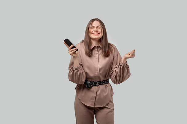 Happy business woman with glasses rejoices in a successful deal. Phone in hand. - Foto, afbeelding