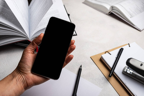 smartphone con pantalla en blanco en la mano sobre el espacio de trabajo con libros
. - Foto, Imagen