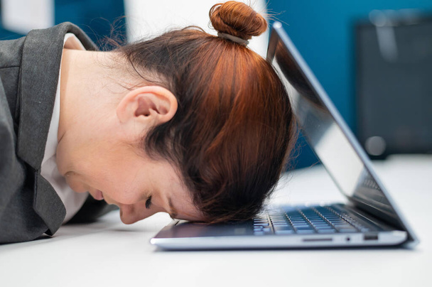 Εξαντλημένη απογοητευμένη επιχειρηματίας έβαλε το κεφάλι της κάτω σε ένα σημειωματάριο που κάθεται σε ένα γραφείο. Μια υπάλληλος δούλευε υπερωρίες και αποκοιμήθηκε σε έναν υπολογιστή στο γραφείο. Σκληρός εργαζόμενος. - Φωτογραφία, εικόνα