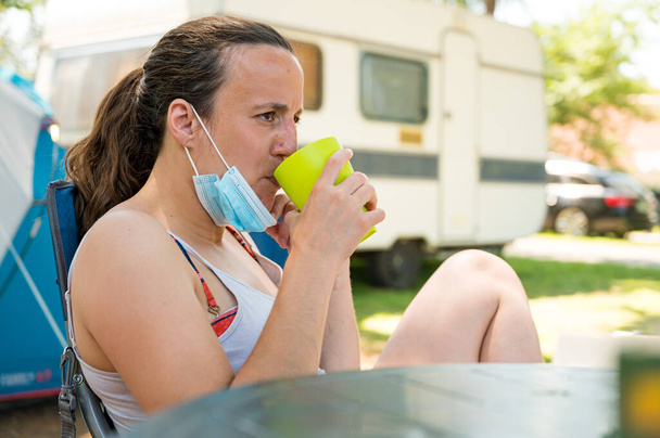 Mulher usando máscara médica beber um refresco no resort de campismo
. - Foto, Imagem