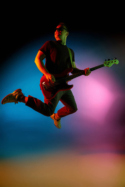 Young caucasian musician playing on gradient background in neon light. Concept of music, hobby, festival - Foto, immagini