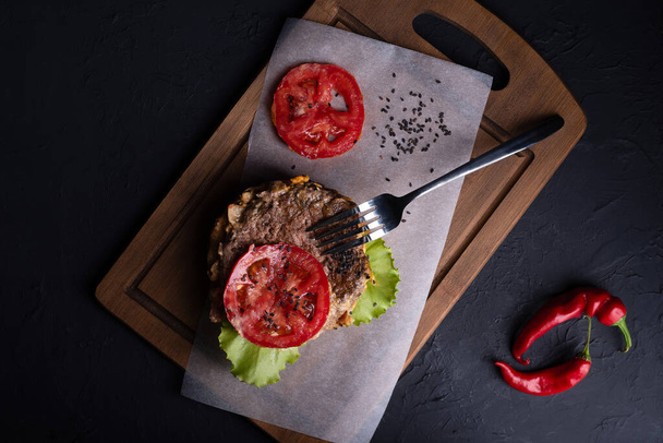 top view, inside burger, meat cutlet with chopped tomatoes,  wooden board, red hot pepper lies next to it, - Photo, image