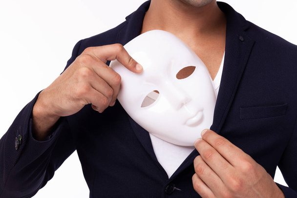 Twee gezichten van Zakenman verbergen wit masker en zet kunstmatige masker op zak pak. Een kantoorbediende is een oneerlijke man. Bedrieglijke man verraadt zakenpartner, oneerlijk verstopt in masker. Jongeman is spion - Foto, afbeelding