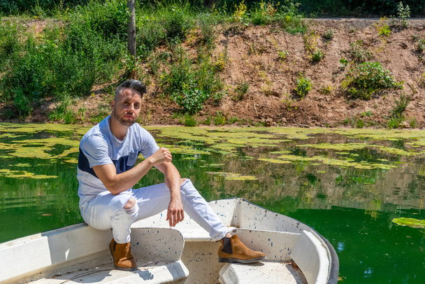 Joven en pantalones blancos y estilo moderno posando en el estanque de agua dulce de Clot De La Mare De Deu en Burriana. Concepto de moda
 - Foto, Imagen